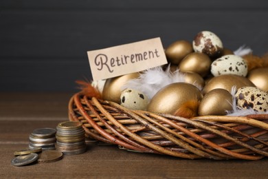 Photo of Card with word Retirement, many golden and quail eggs in nest on wooden table. Pension concept