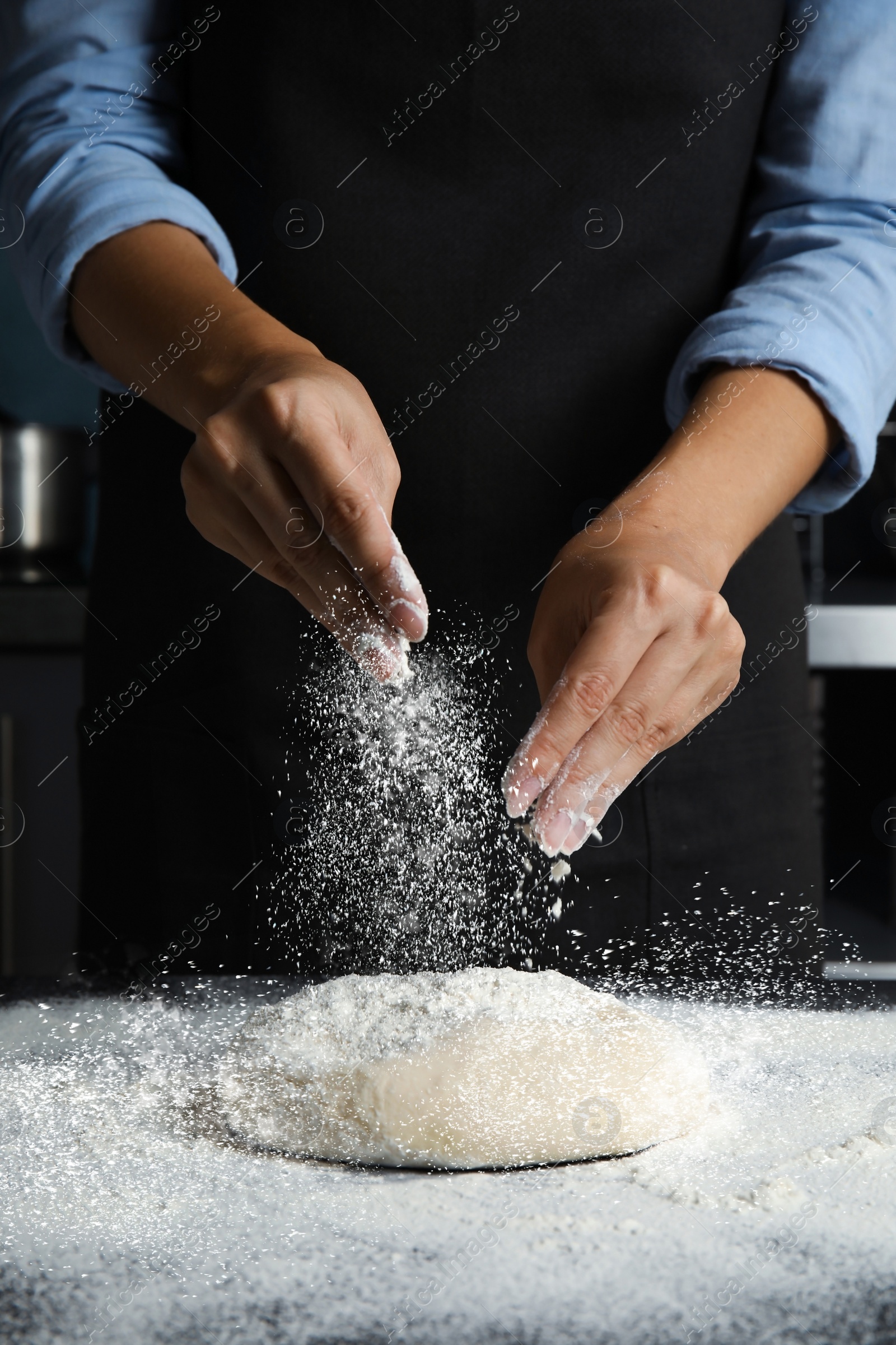 Image of Woman sprinkling flour over dough on table in kitchen, closeup