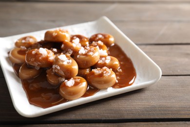 Photo of Plate with tasty candies, caramel sauce and salt on wooden table, closeup