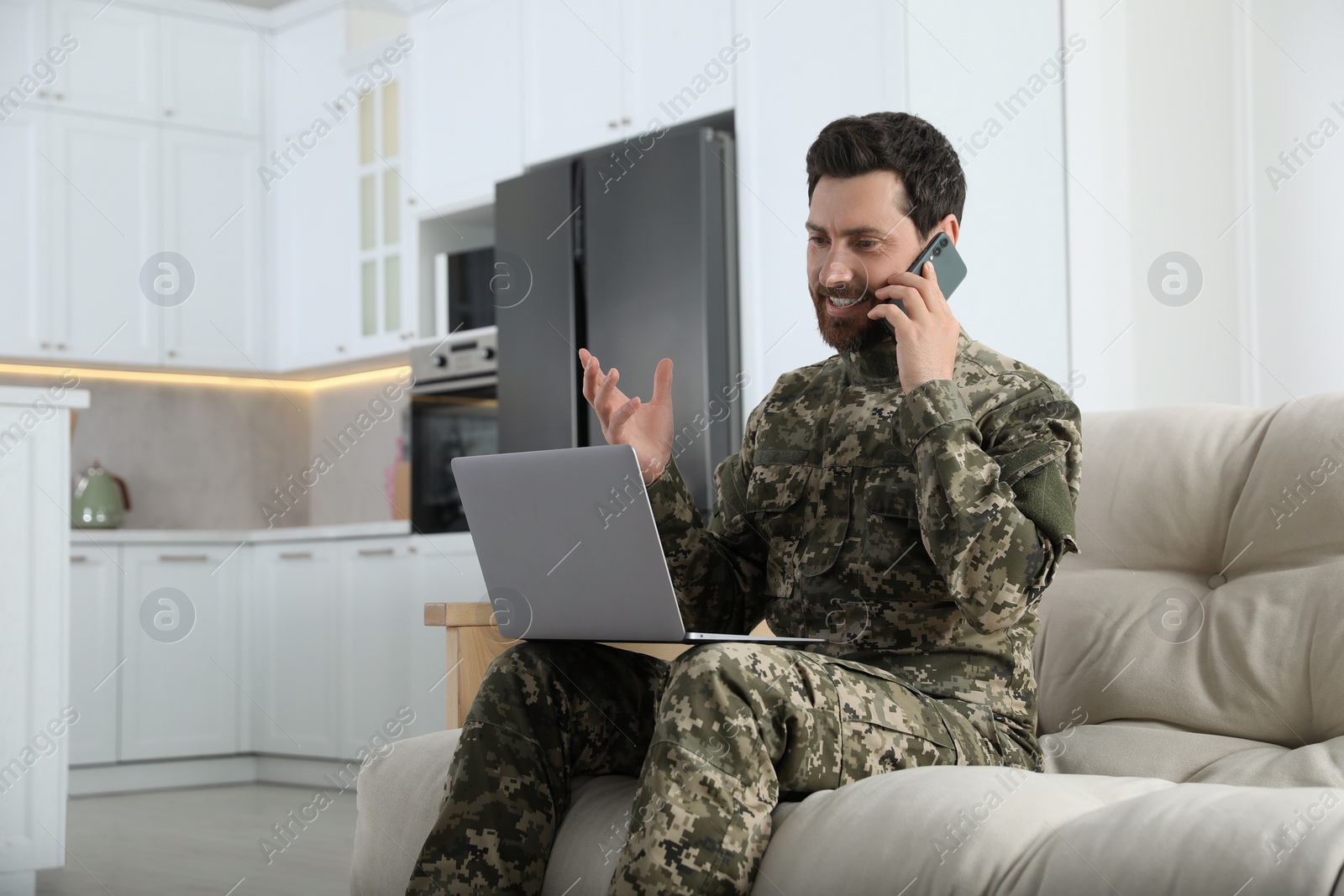 Photo of Soldier with laptop talking on phone at home. Military service