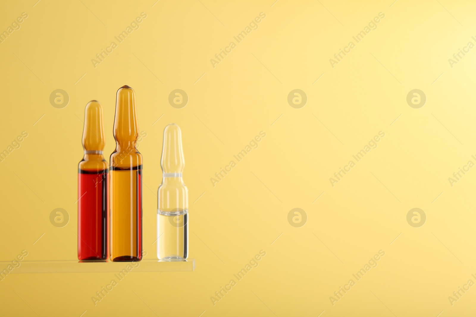 Photo of Glass ampoules with liquid on yellow background. Space for text