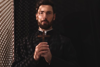 Catholic priest in cassock holding cross in confessional