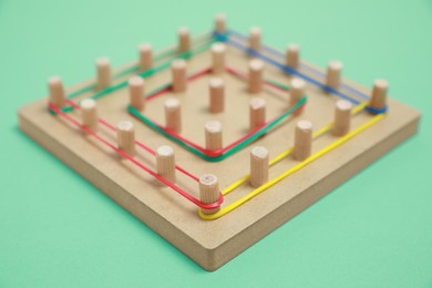 Photo of Wooden geoboard with rubber bands on green background, closeup. Educational toy for motor skills development