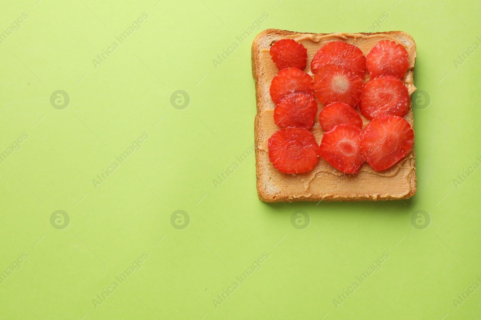 Photo of Tasty peanut butter sandwich with sliced strawberries on light green background, top view. Space for text