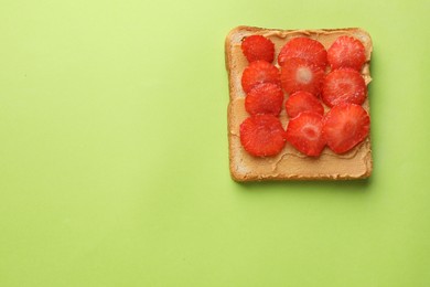 Photo of Tasty peanut butter sandwich with sliced strawberries on light green background, top view. Space for text