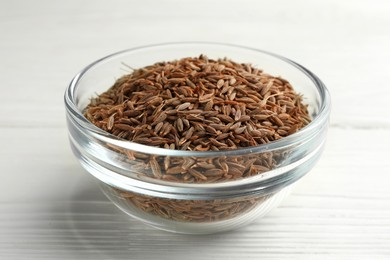 Bowl of caraway seeds on white wooden table, closeup