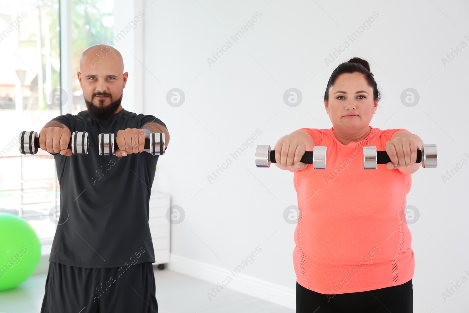 Photo of Overweight man and woman doing exercise with dumbbells in gym