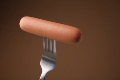 Photo of Delicious boiled sausage on fork against brown background, closeup