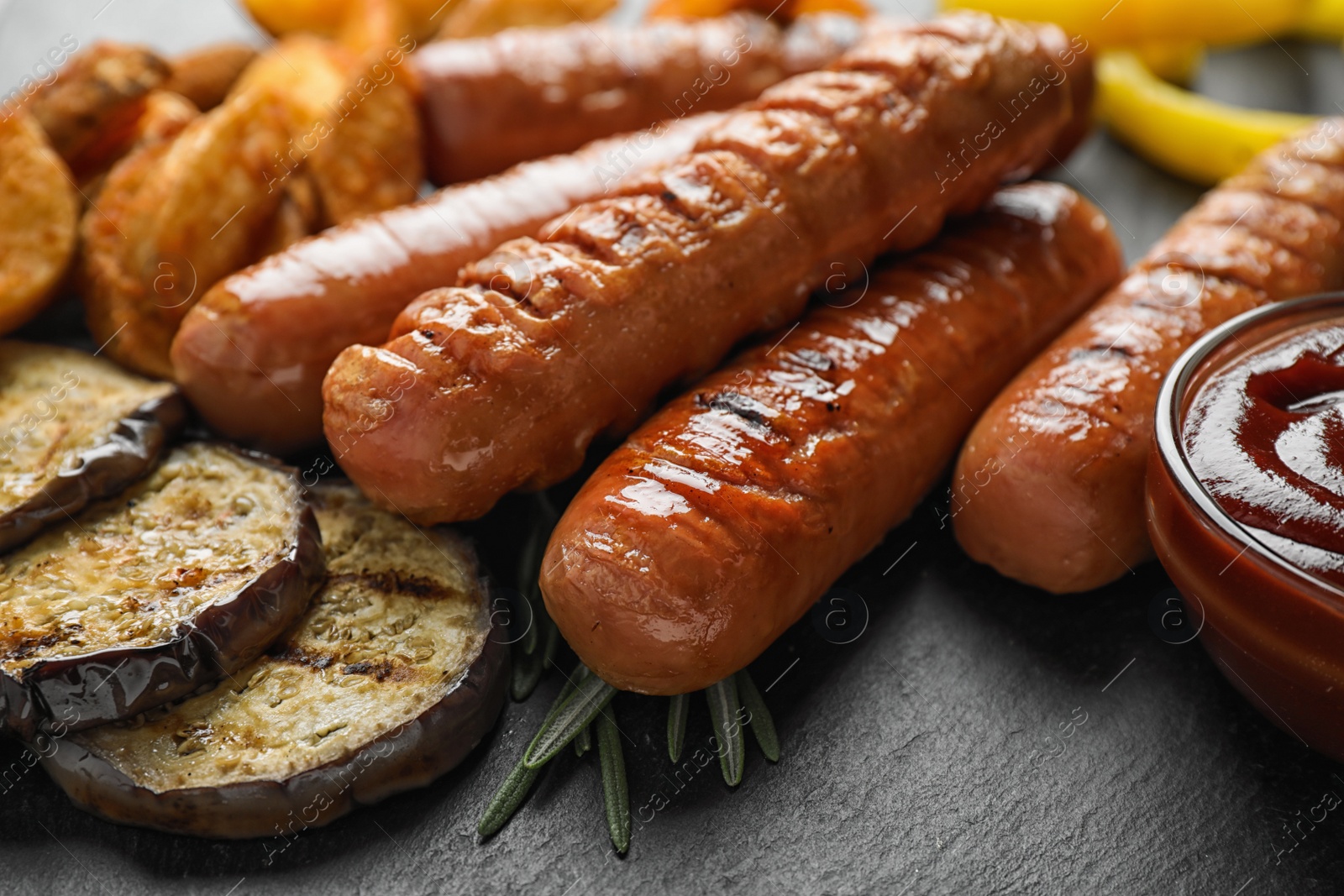 Photo of Delicious grilled sausages and vegetables on slate plate, closeup. Barbecue food