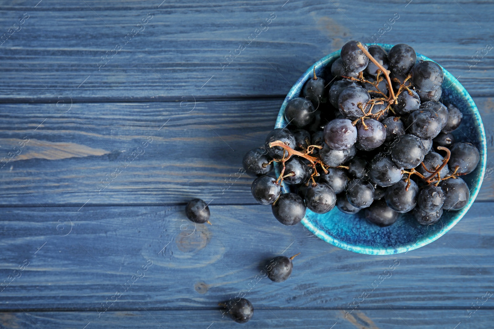 Photo of Fresh ripe juicy grapes in bowl and space for text on wooden background, top view