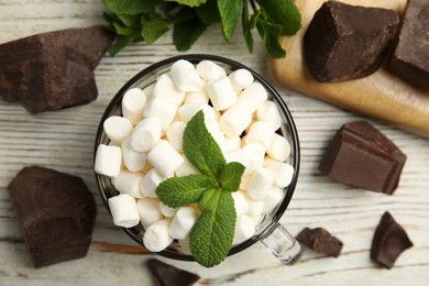 Photo of Glass cup of delicious hot chocolate with marshmallows and fresh mint on white wooden table flat lay