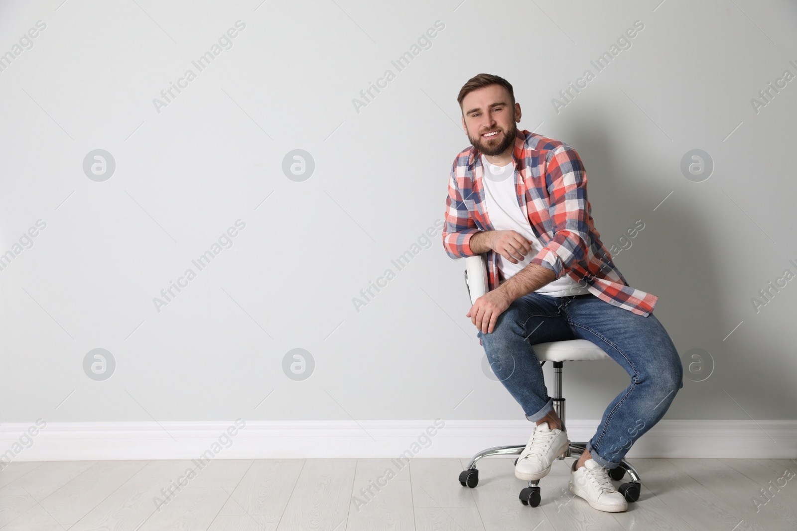 Photo of Young man sitting in comfortable office chair near white wall indoors, space for text
