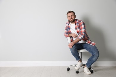 Young man sitting in comfortable office chair near white wall indoors, space for text