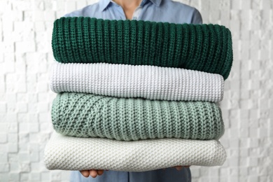 Photo of Woman holding stack of warm clothes on white background, closeup. Autumn season