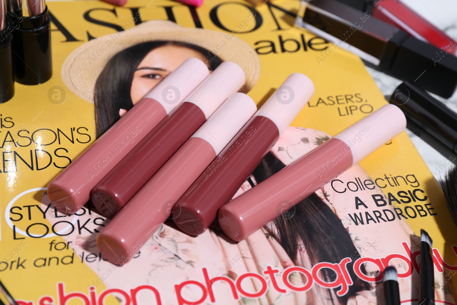 Photo of Bright lip glosses and fashion magazine on table, closeup