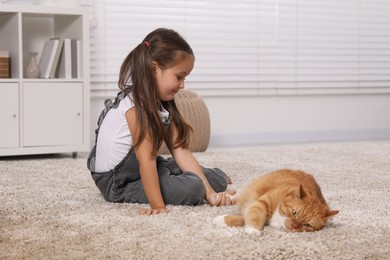 Photo of Little girl and cute ginger cat on carpet at home