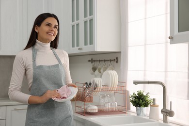 Photo of Happy woman wiping bowl with towel in kitchen, space for text