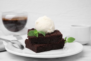 Photo of Tasty brownies served with ice cream and mint on white marble table, closeup