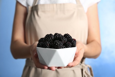 Photo of Woman holding bowl of fresh blackberry against color background, closeup