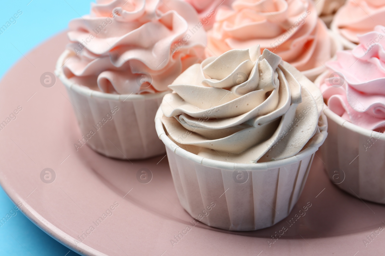 Photo of Plate with tasty cupcakes on light blue background, closeup