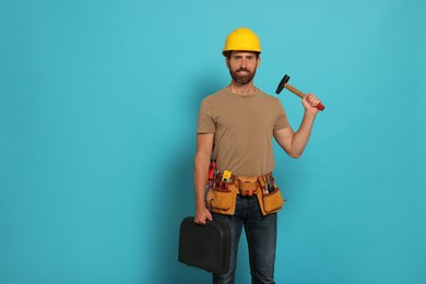 Professional builder in hard hat with hammer and tool belt on light blue background