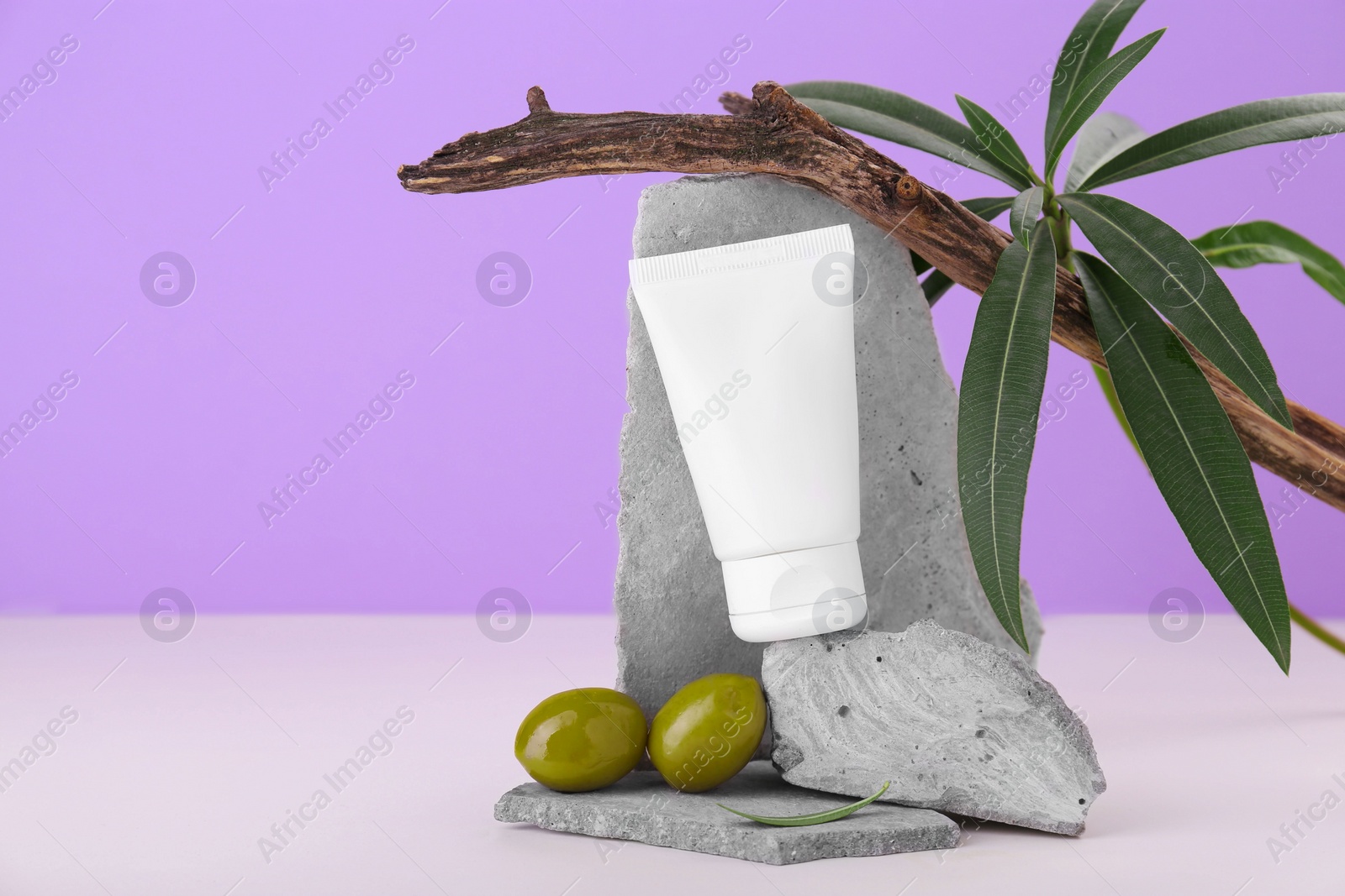 Photo of Tube of natural cream and olives on stones against purple background. Space for text