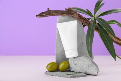 Photo of Tube of natural cream and olives on stones against purple background. Space for text