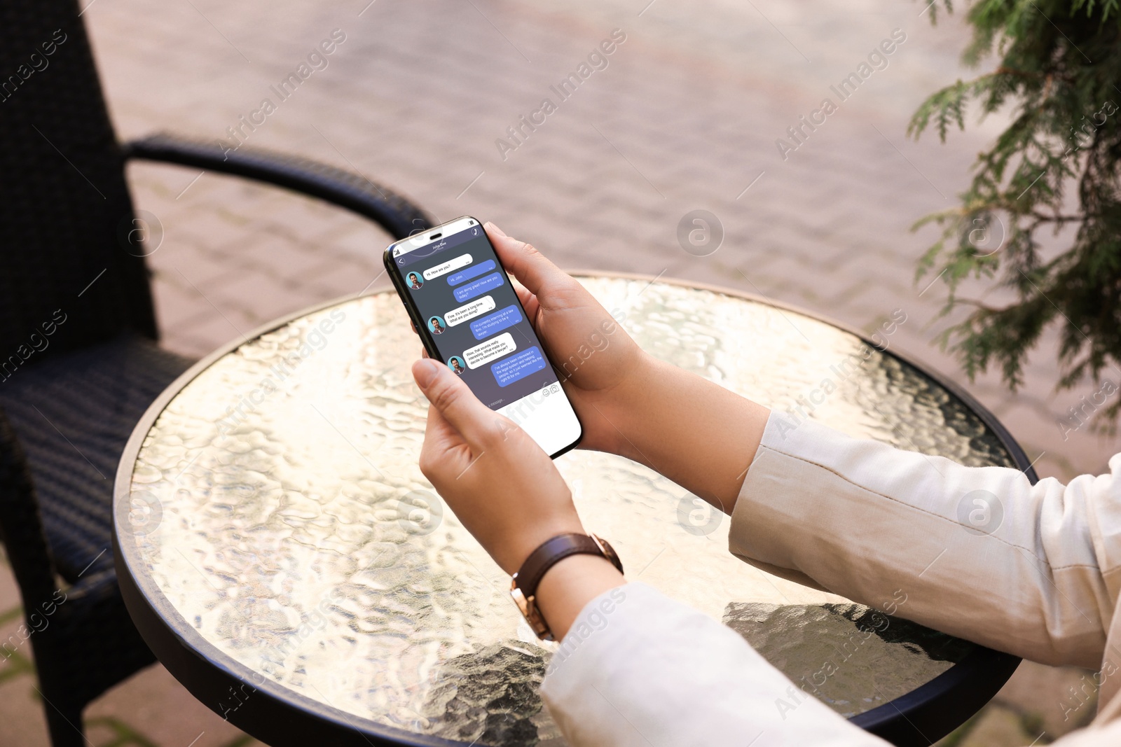 Image of Woman texting via mobile phone at table outdoors, closeup. Device screen with messages