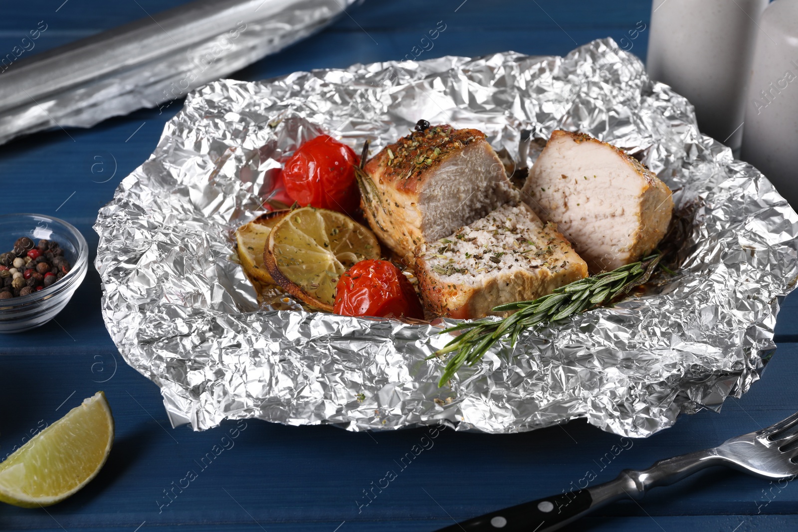 Photo of Pieces of delicious meat baked in foil with tomatoes on blue wooden table