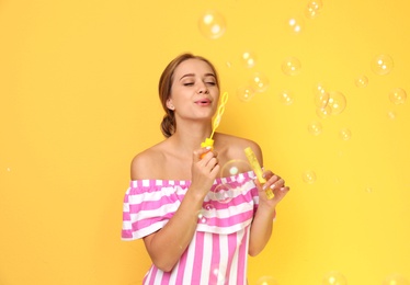 Young woman blowing soap bubbles on color background