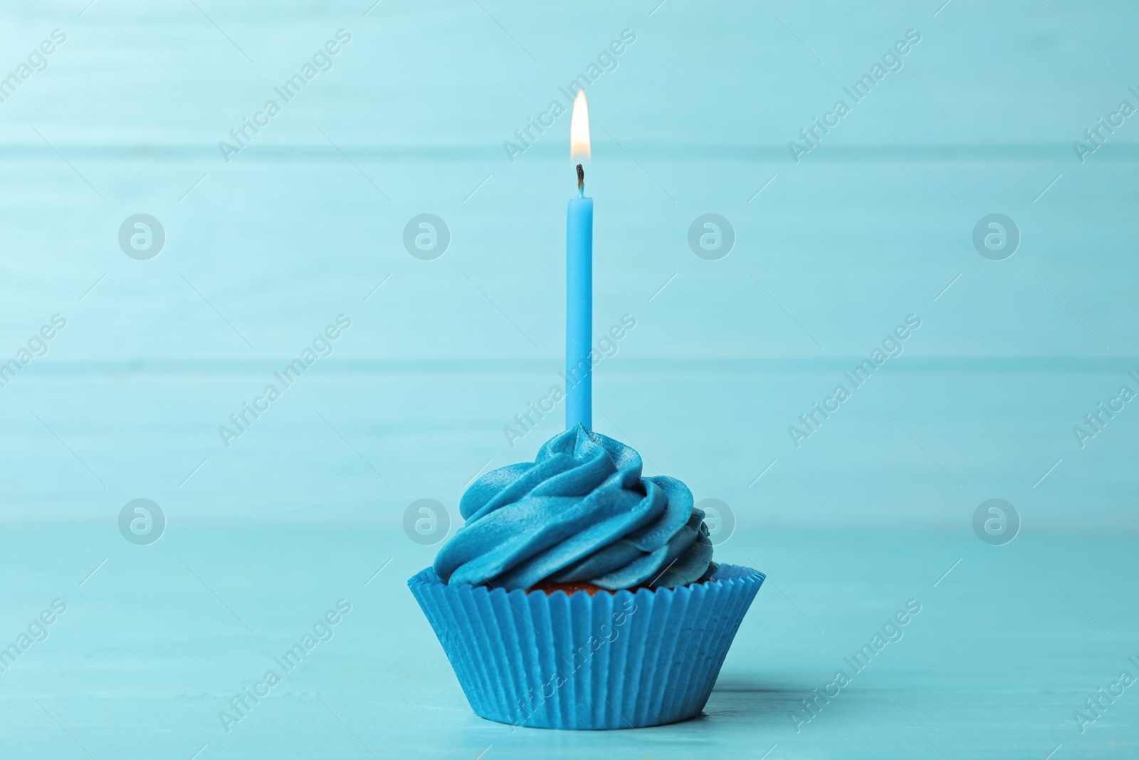 Photo of Delicious birthday cupcake with cream and burning candle on blue wooden background