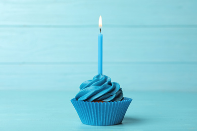 Delicious birthday cupcake with cream and burning candle on blue wooden background