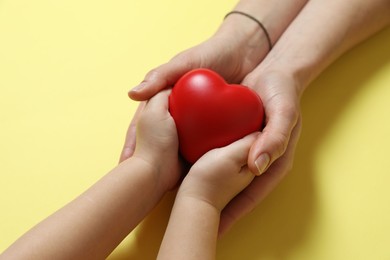 Mother and her child holding red decorative heart on pale yellow background, closeup