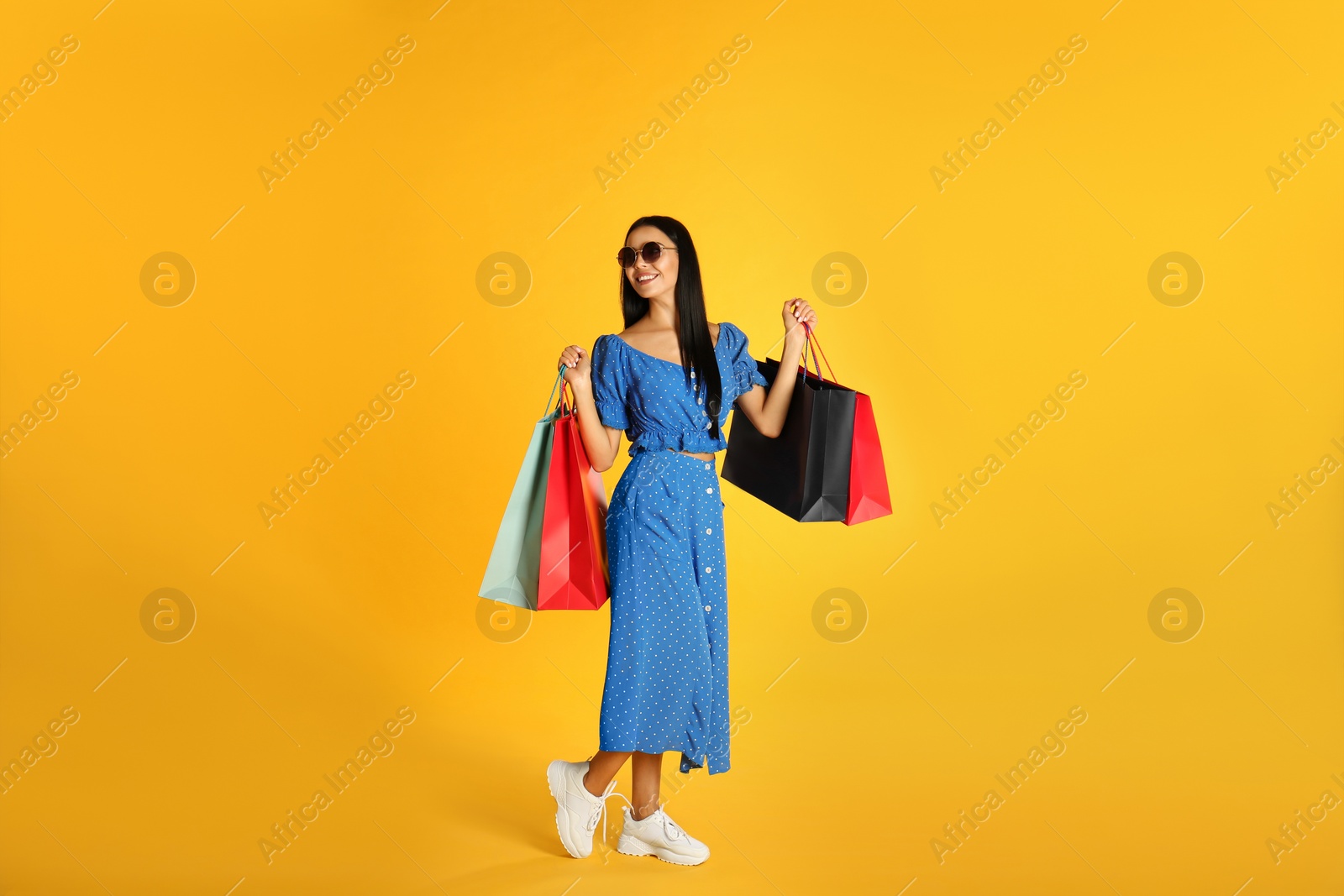 Photo of Beautiful young woman with paper shopping bags on yellow background