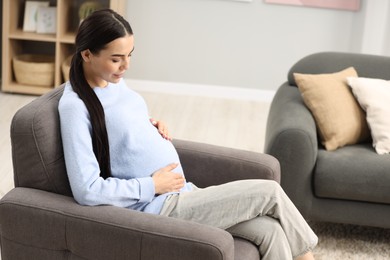 Pregnant young woman on armchair at home