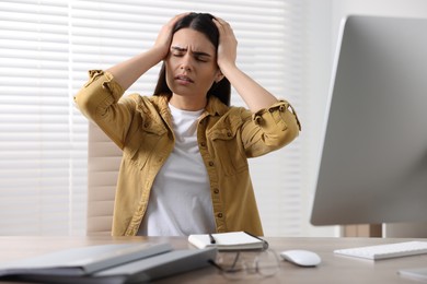 Photo of Young woman suffering from headache at wooden table in office