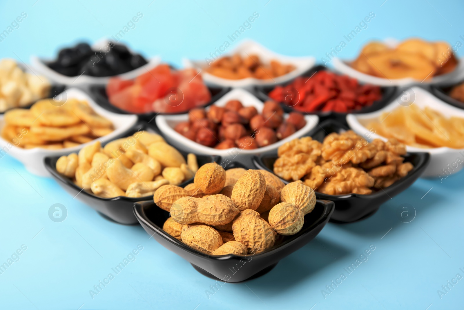 Photo of Bowls with dried fruits and nuts on light blue background, closeup