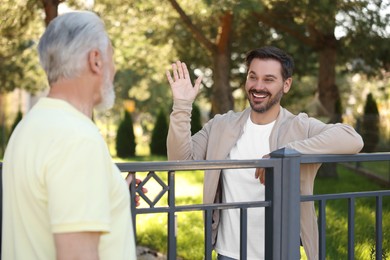 Photo of Friendly relationship with neighbours. Happy men near fence outdoors