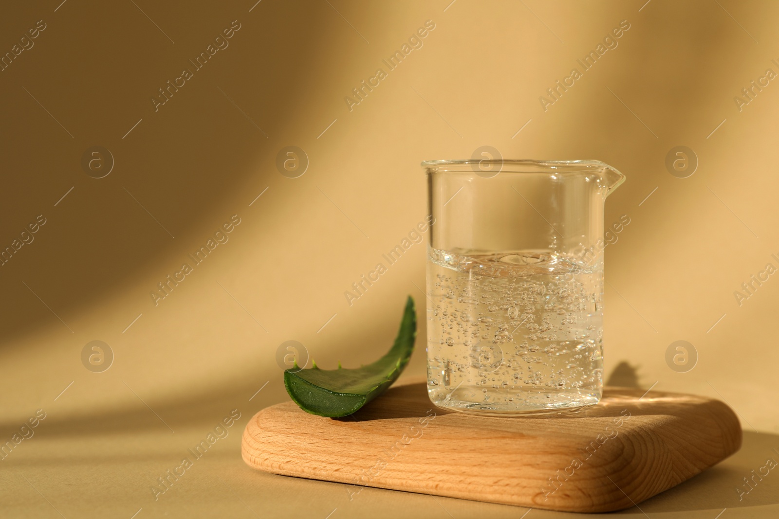 Photo of Glass beaker of cosmetic gel and aloe on yellow background, space for text