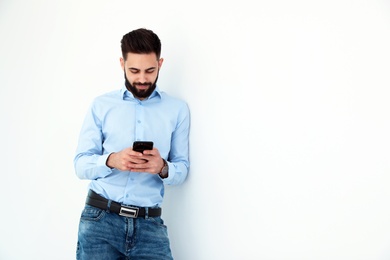 Handsome young man using phone near white wall, space for text. Working time