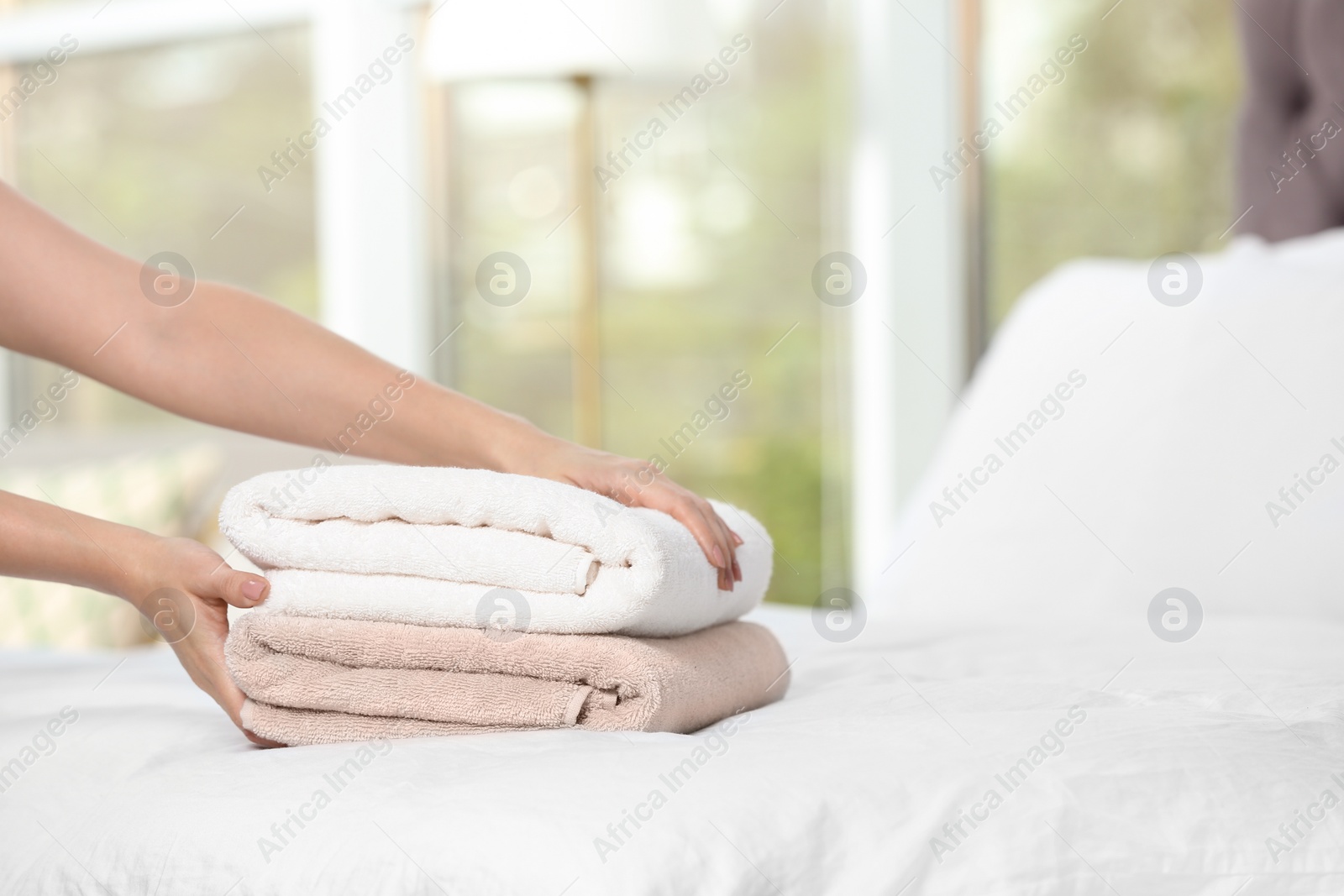 Photo of Woman putting soft clean towels onto bed, closeup. Space for text