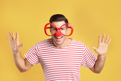 Funny man with clown nose and large glasses on yellow background. April fool's day