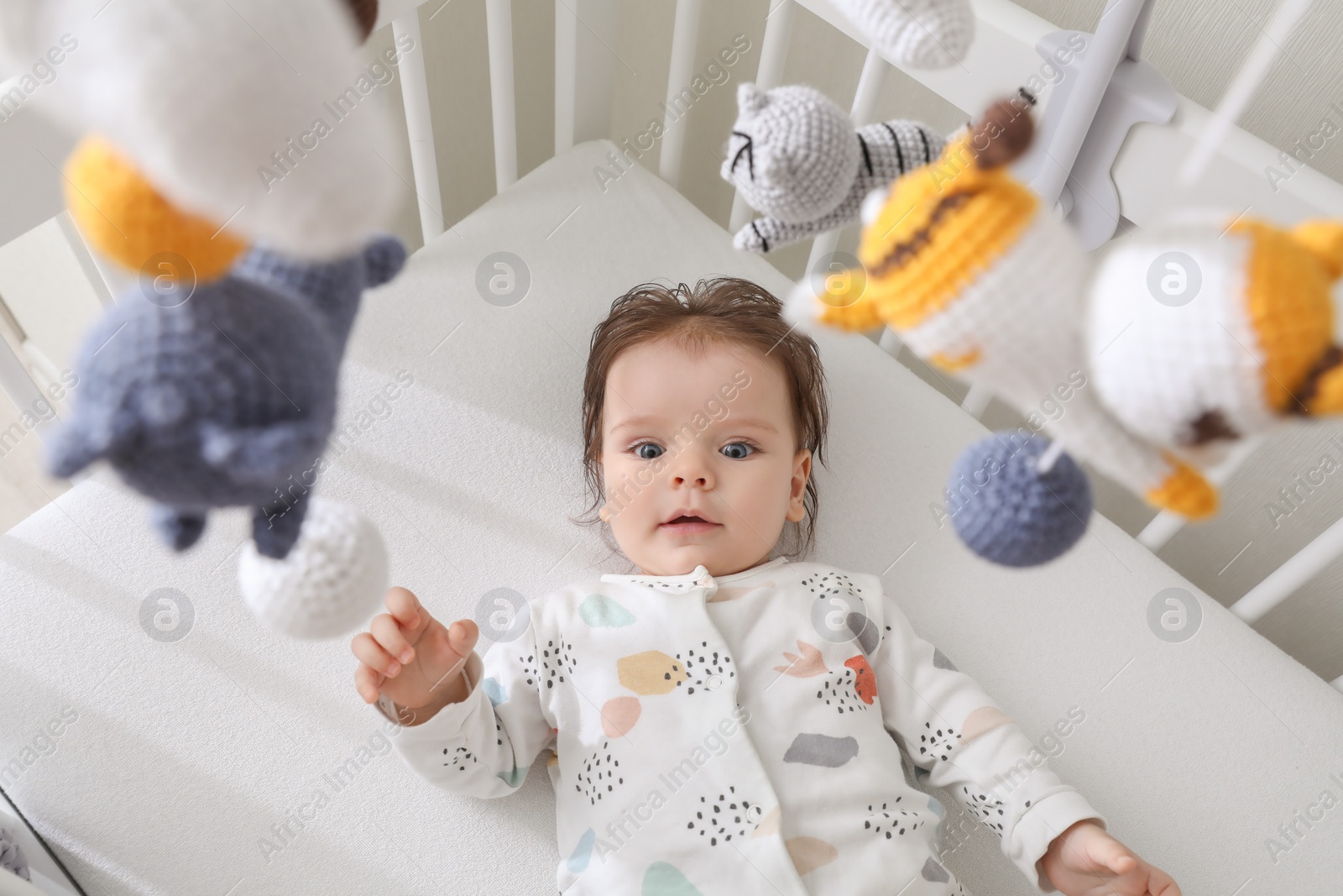 Photo of Cute little baby looking at hanging mobile in crib, above view