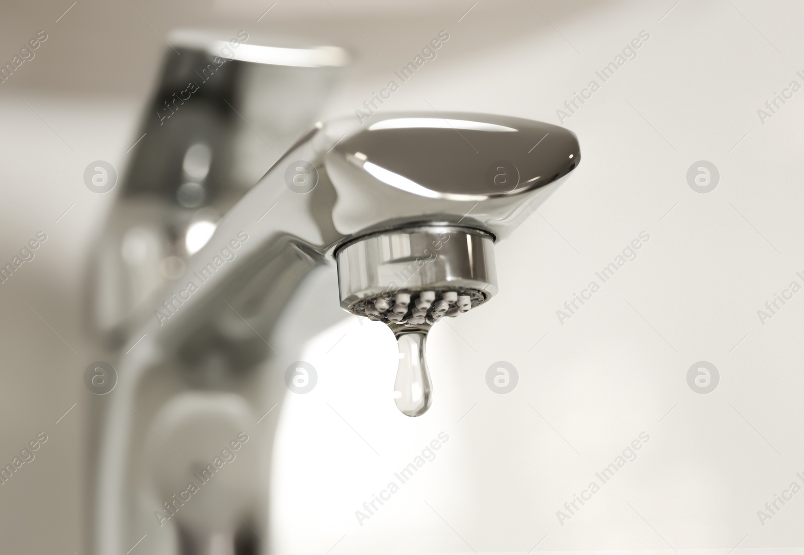 Photo of Water drop falling down from tap on light background, closeup