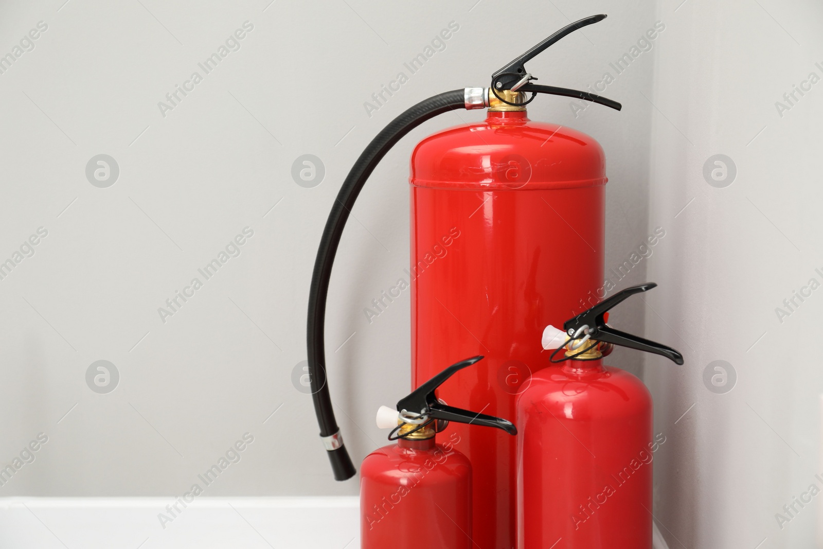 Photo of Three fire extinguishers near light grey wall