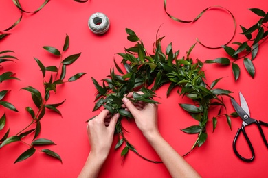 Florist making beautiful mistletoe wreath on red background, top view. Traditional Christmas decor