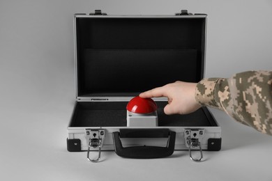 Photo of Serviceman pressing red button of nuclear weapon on light gray background, closeup. War concept
