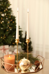 Photo of Burning candles and fir branch on table in room decorated for Christmas