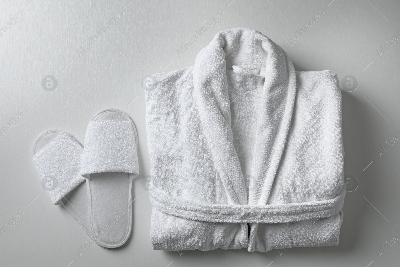 Photo of Clean folded bathrobe and slippers on white background, flat lay