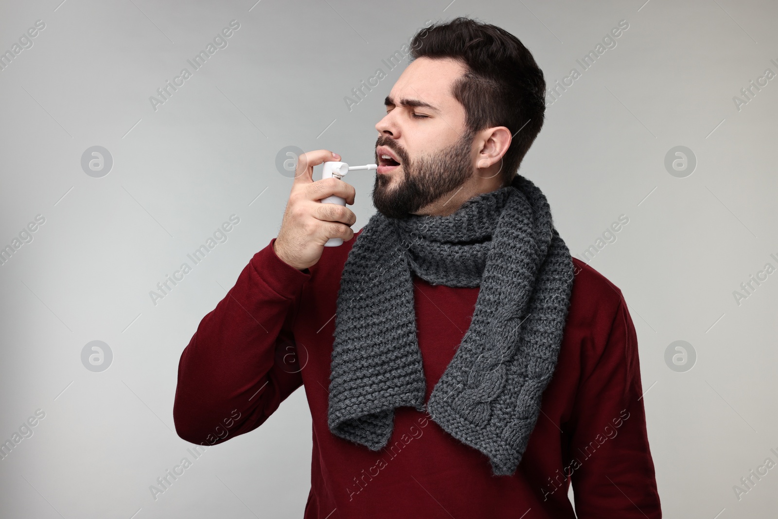 Photo of Young man with scarf using throat spray on grey background